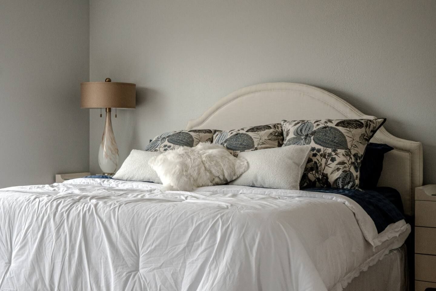 A bed with white sheets and pillows in a bedroom with a lamp.