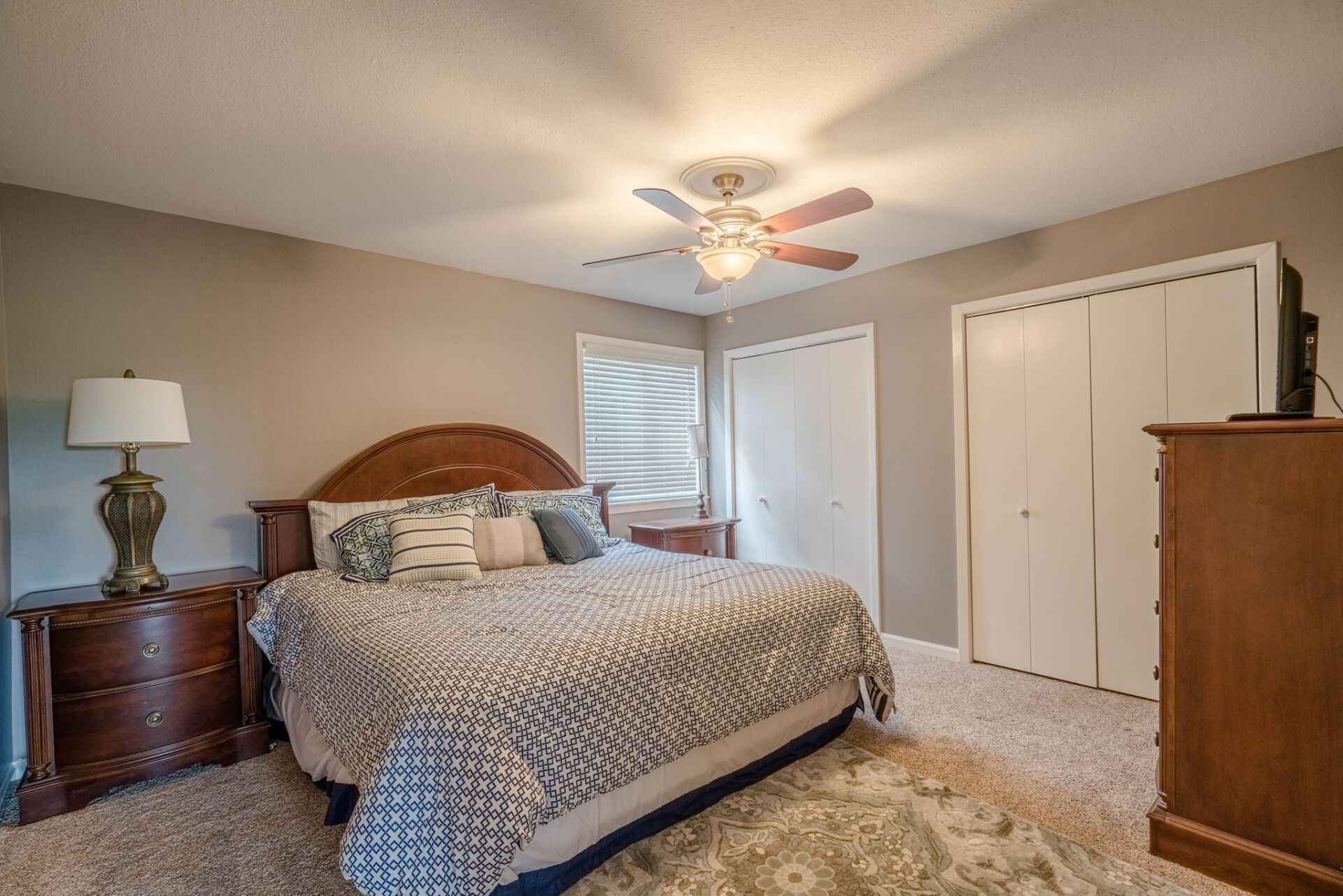 A bedroom with a king size bed , nightstand , dresser and ceiling fan.