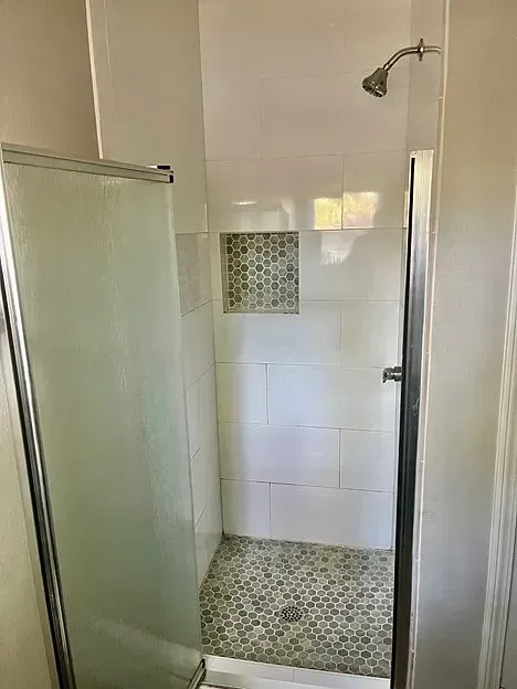 A bathroom with a walk in shower with a glass door and a shower head.