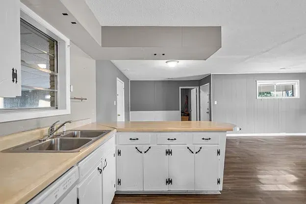 A kitchen with white cabinets , a sink , and a window.