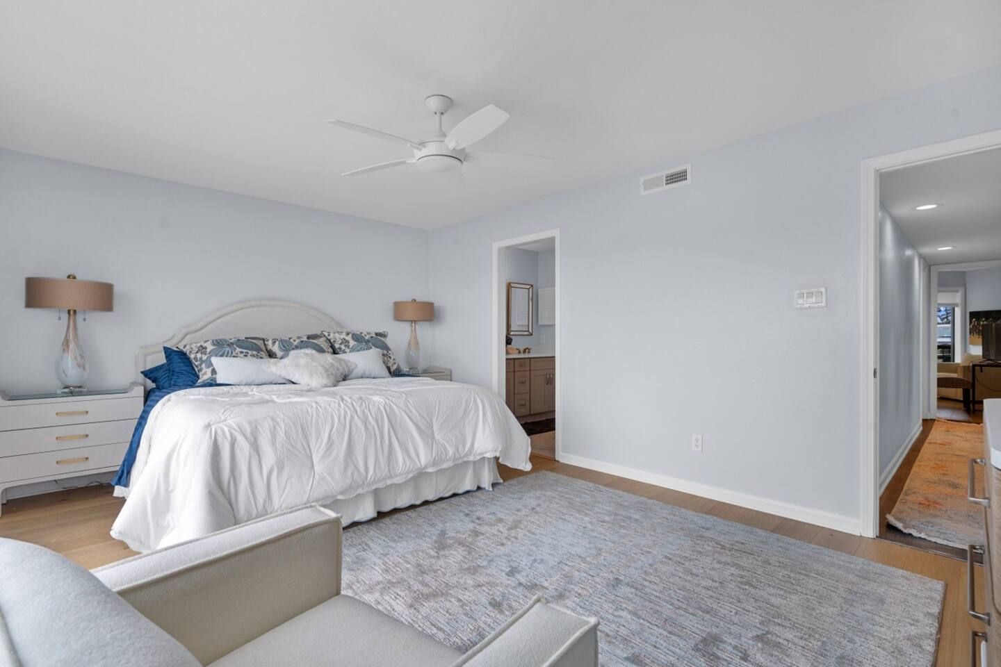 A bedroom with a king size bed , chair , rug and ceiling fan.
