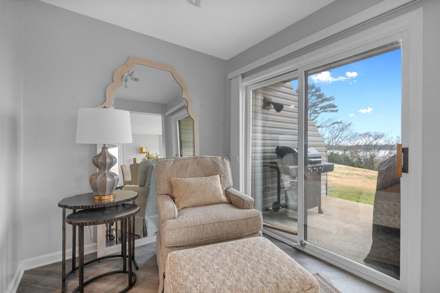A living room with a chair , ottoman , table and mirror.