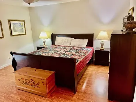 Bedroom with dark wooden sleigh bed, two nightstands with lamps, wooden dresser, and chest.