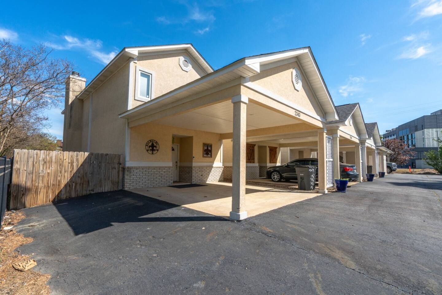 A car is parked under a canopy in front of a house.