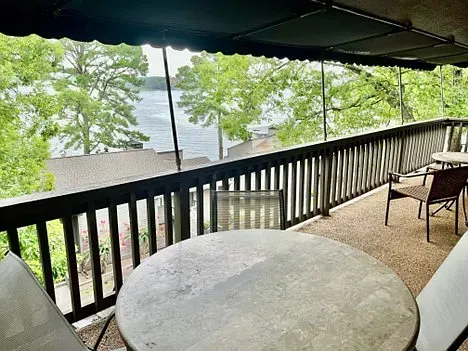 Balcony overlooking a lake with tables and chairs. Dark awning and railing. Trees in the background.