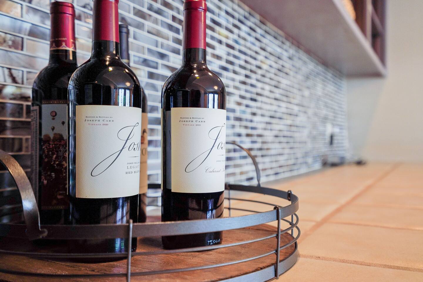 Three bottles of red wine are sitting on a wooden tray.