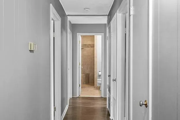 A long hallway with hardwood floors and white doors leading to a bathroom.