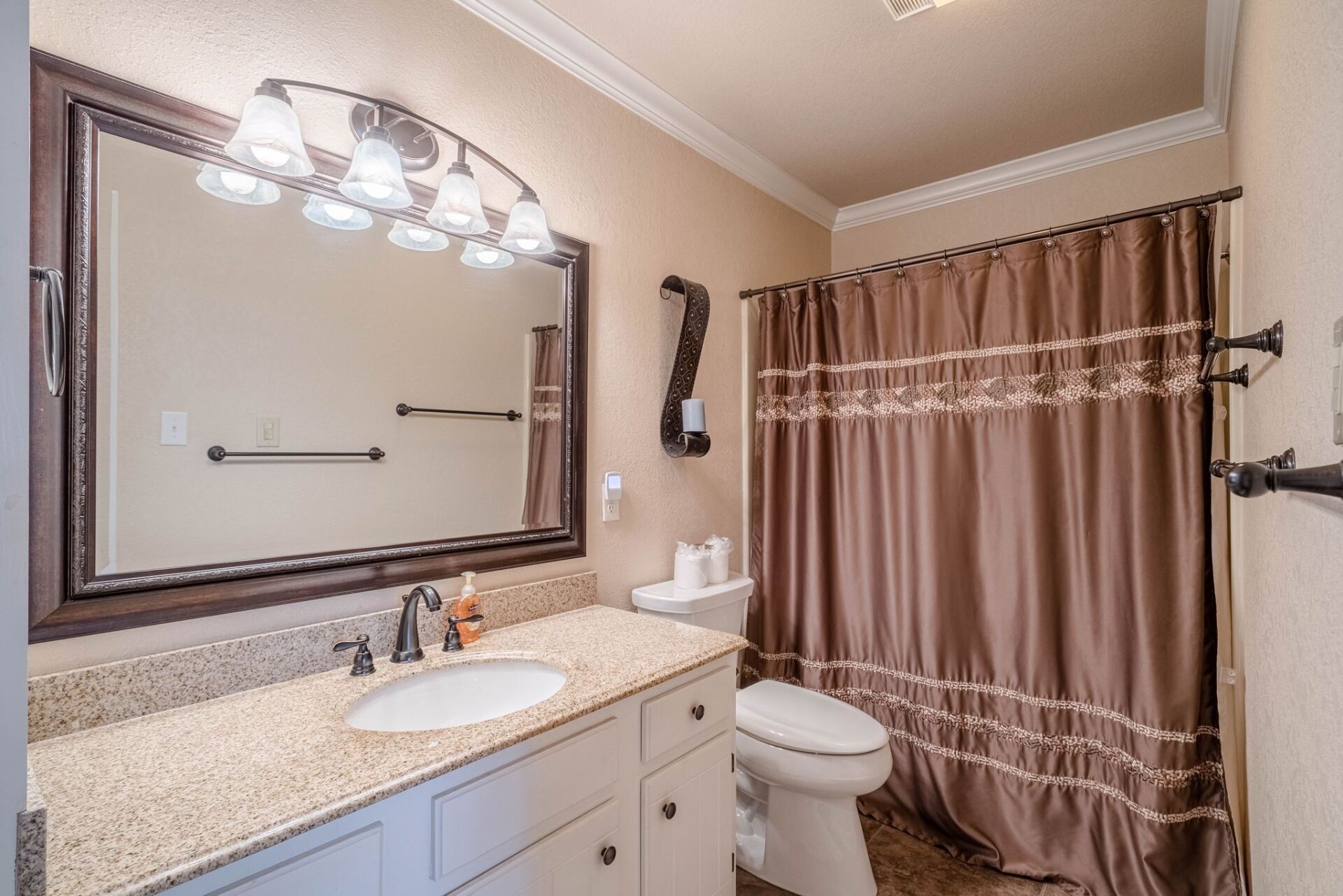 A bathroom with a toilet , sink , mirror and shower curtain.