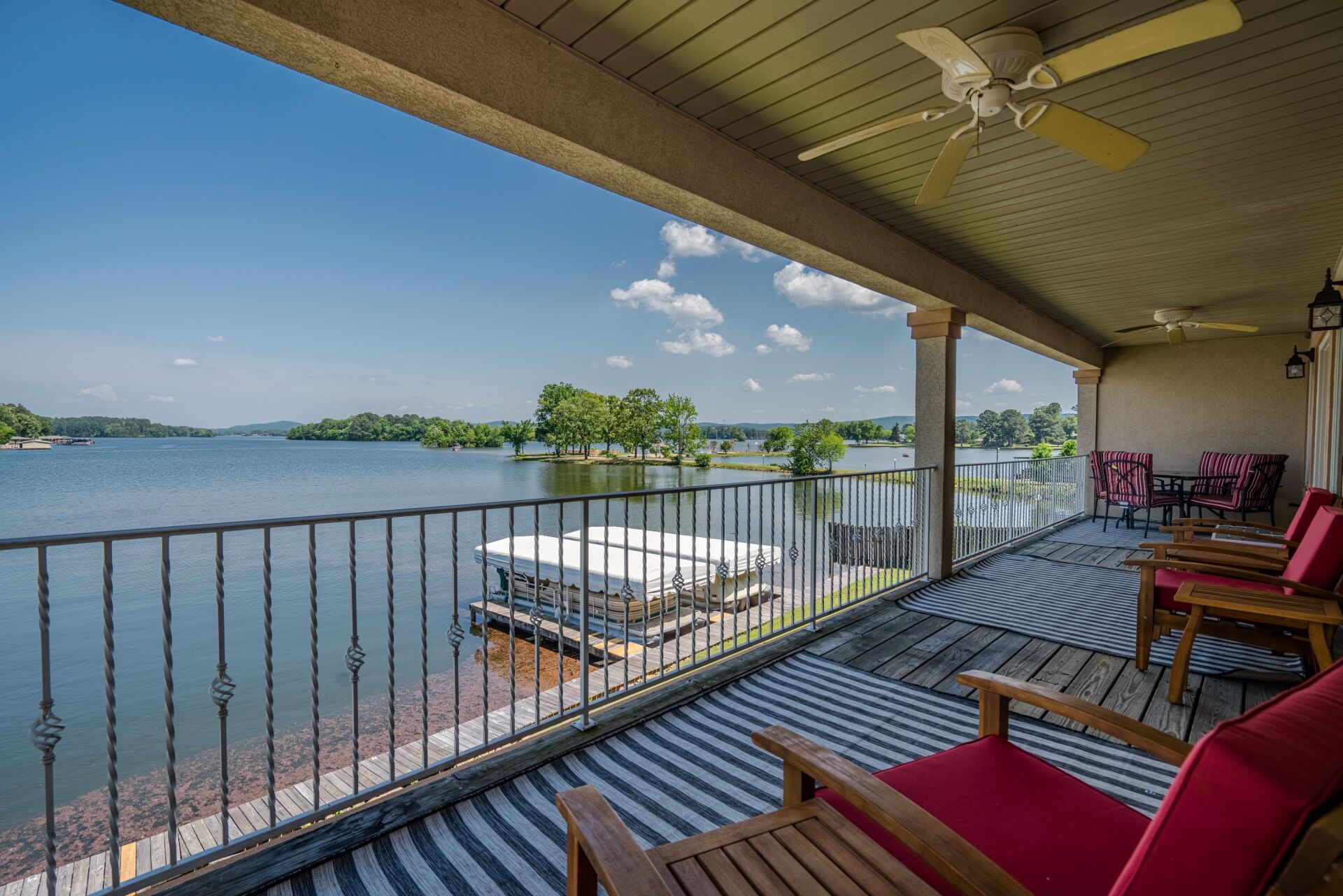 A balcony overlooking a lake with a ceiling fan and chairs.