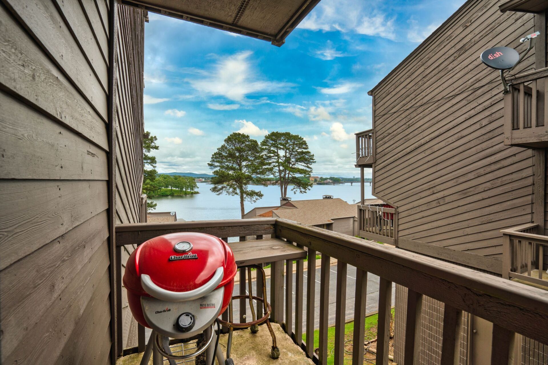 A red grill is sitting on a balcony overlooking a lake.