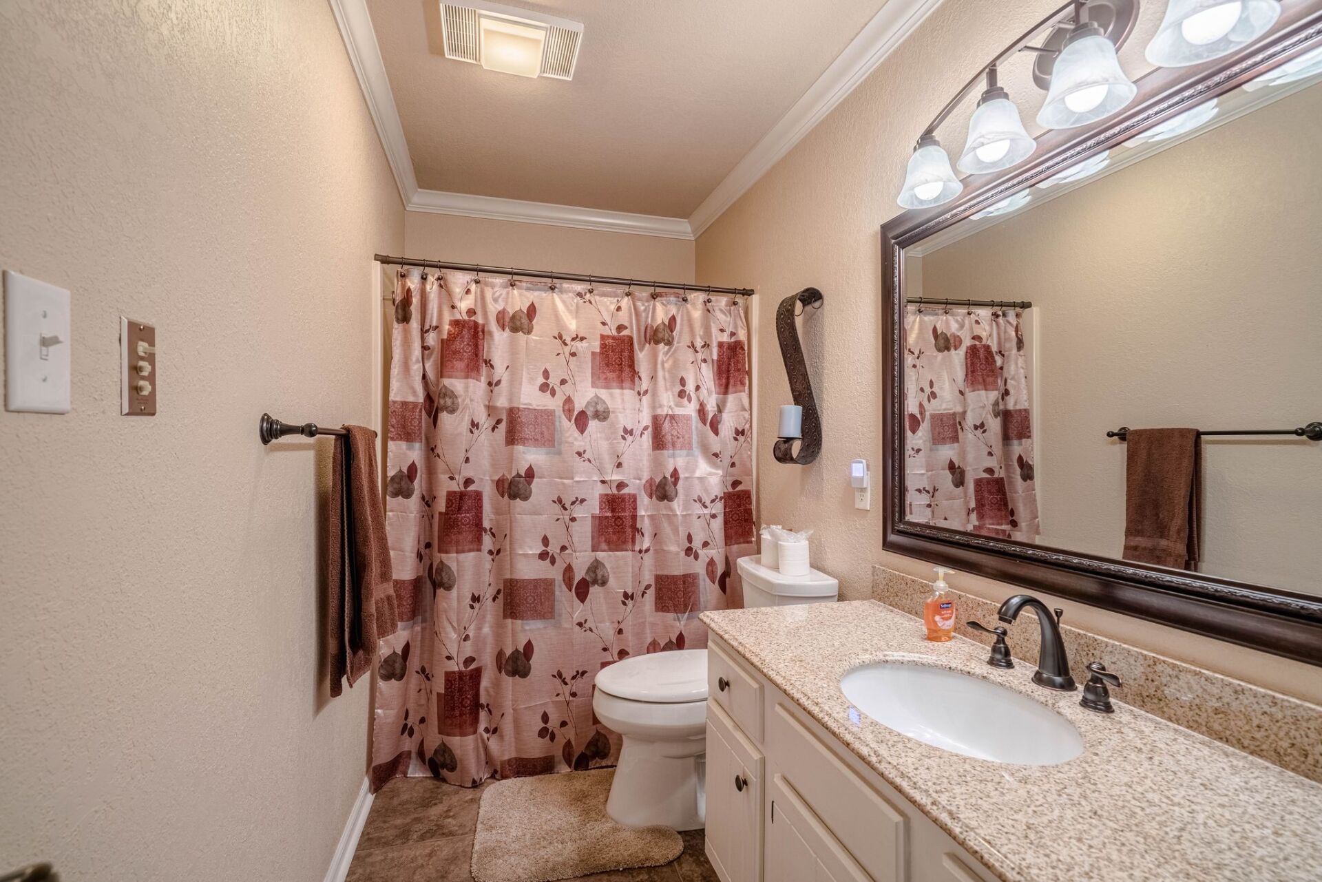 A bathroom with a toilet , sink , mirror and shower curtain.