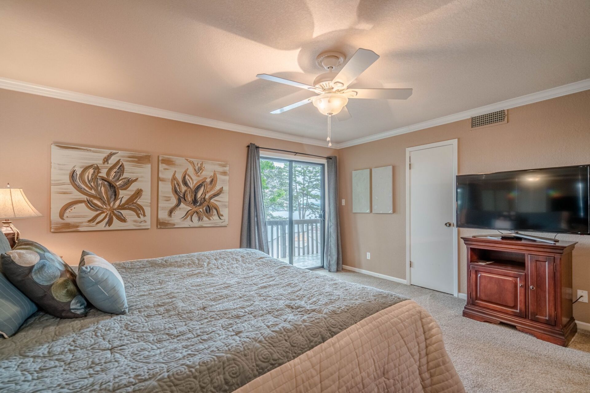 A bedroom with two beds , a ceiling fan , a flat screen tv and a balcony.