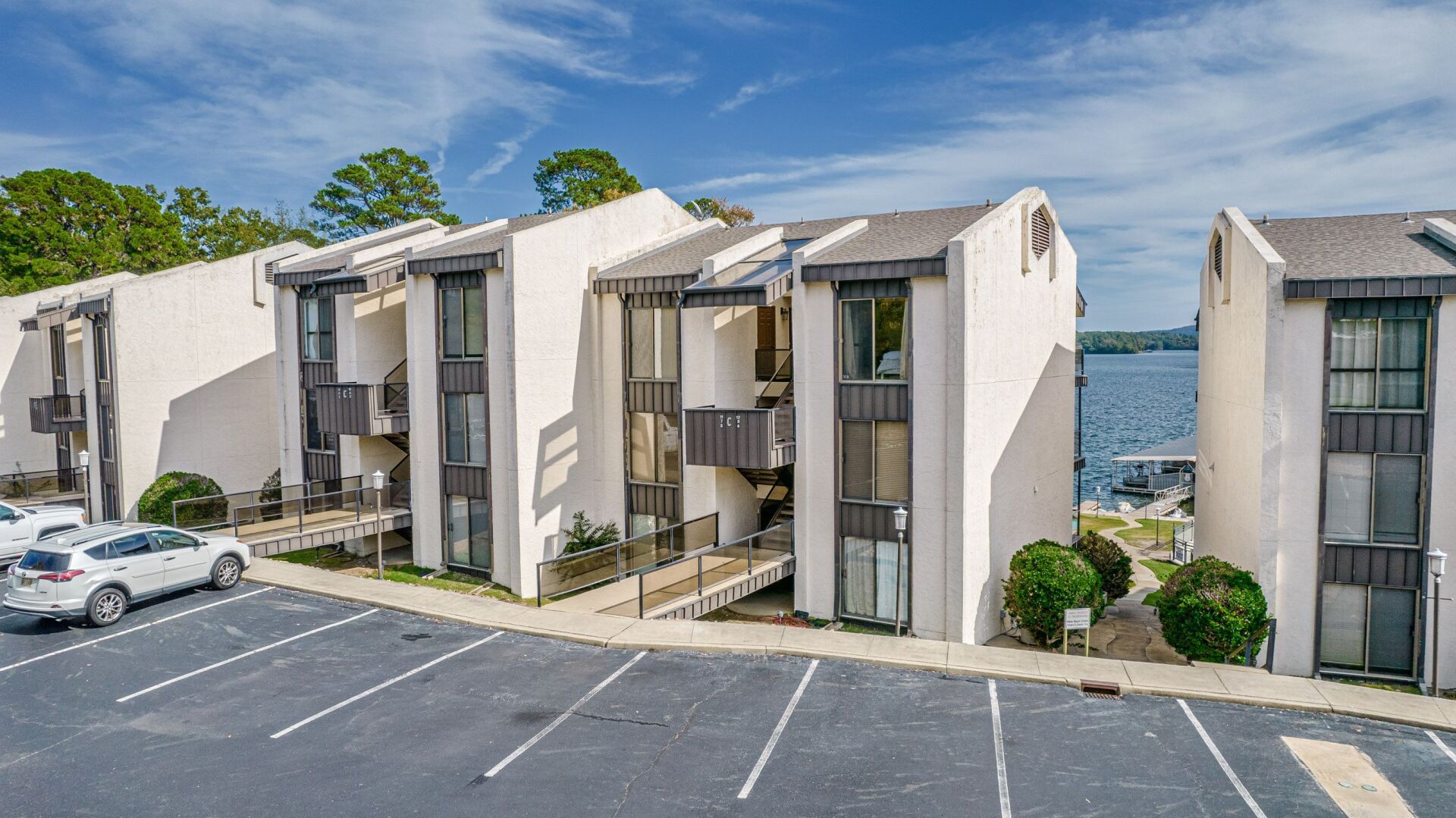 A row of apartment buildings with a parking lot in front of them and a lake in the background.