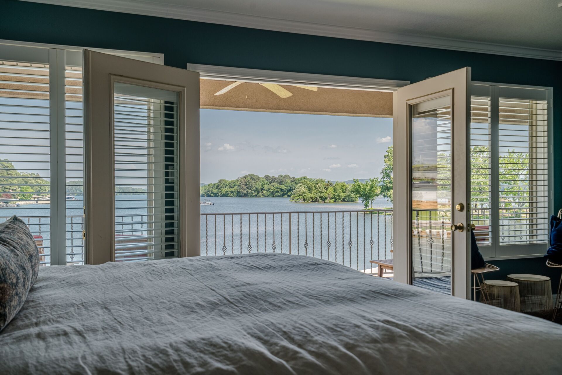 A bedroom with a bed , shutters , and a view of a lake.