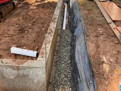 A pipe is laying in the dirt next to a concrete wall.