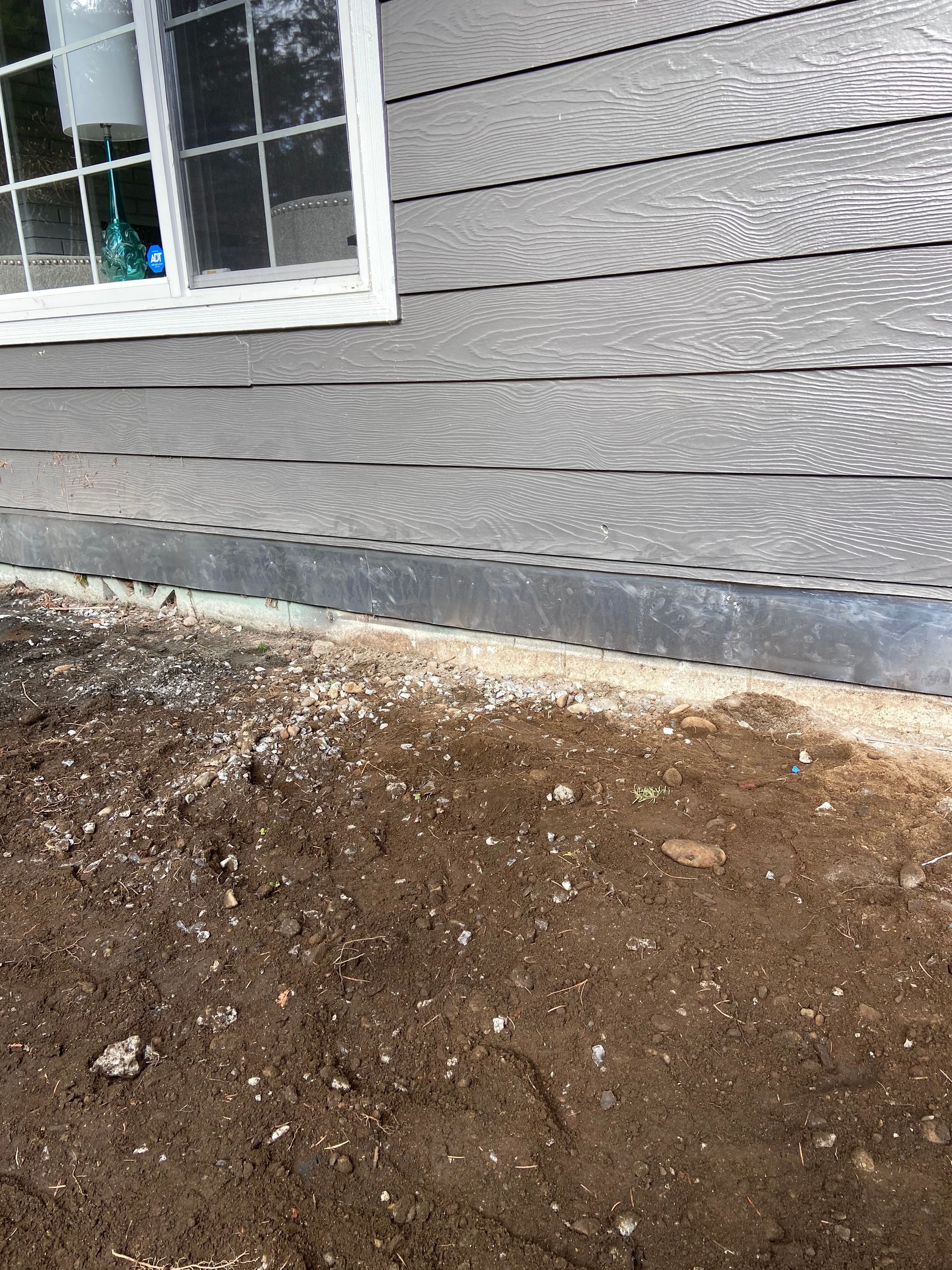 A house with a window and a lot of dirt on the ground in front of it.