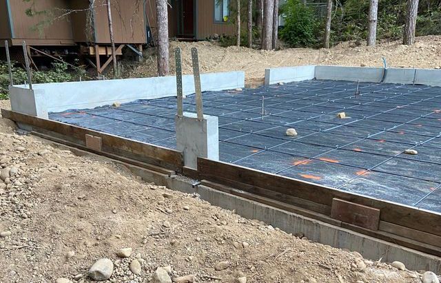 A concrete base for a house is being built in the dirt.