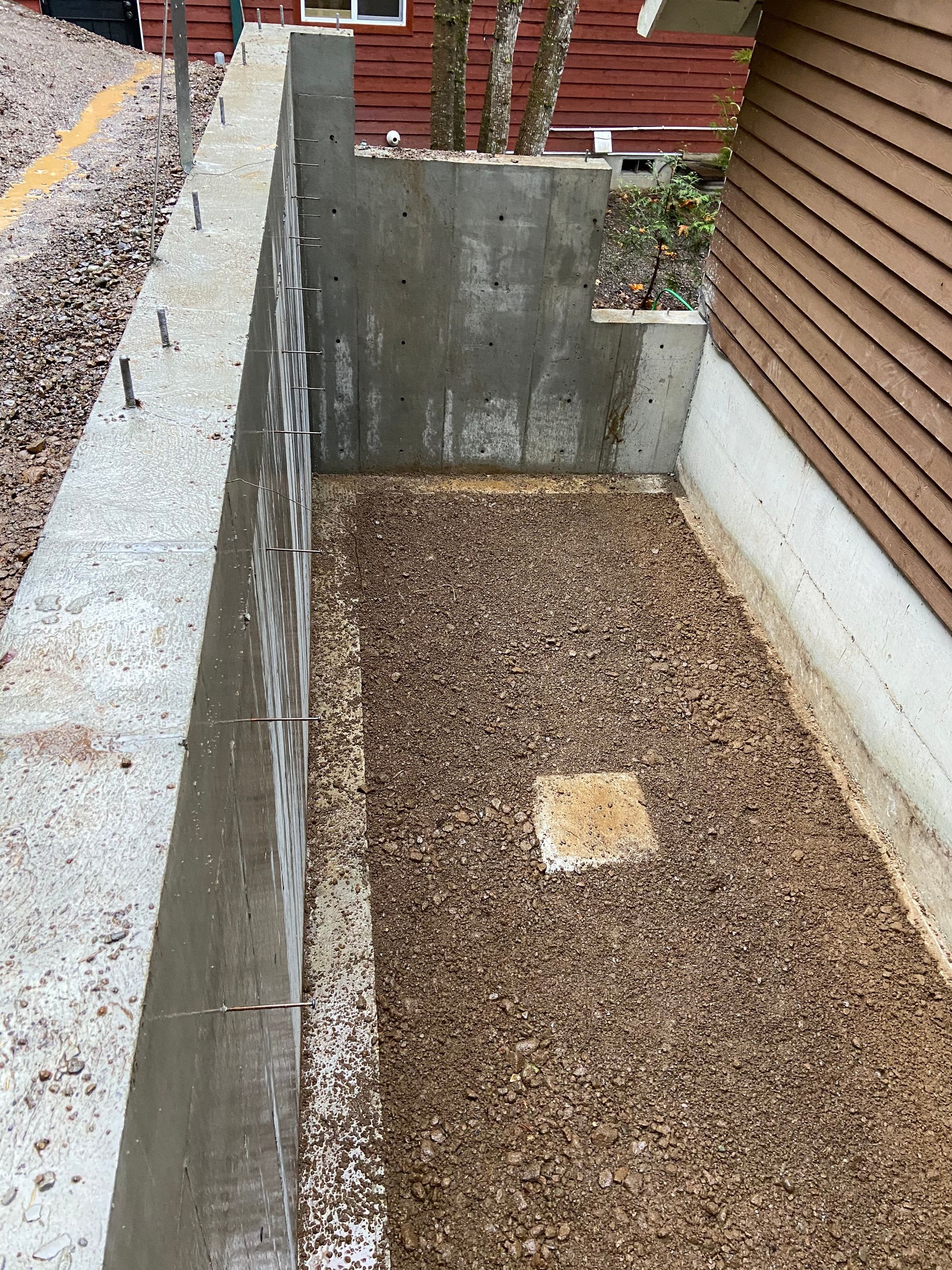 A concrete wall is being built next to a gravel area in front of a house.