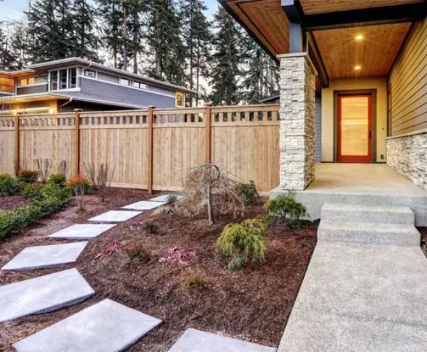 A house with a wooden fence and a concrete walkway leading to the front door.