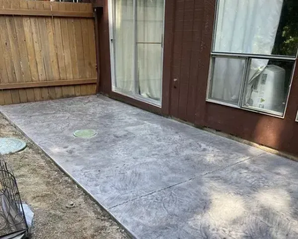 Concrete patio with dark aggregate and painted white stripe. Adjacent to house siding and small brick pile.