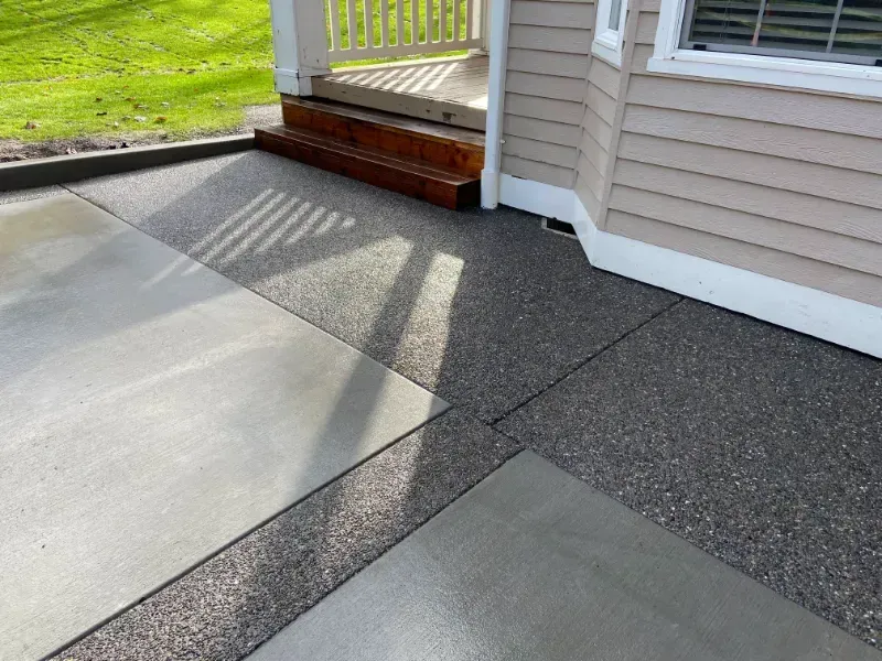 Concrete patio with a decorative stone border, next to a cream-colored house and steps.