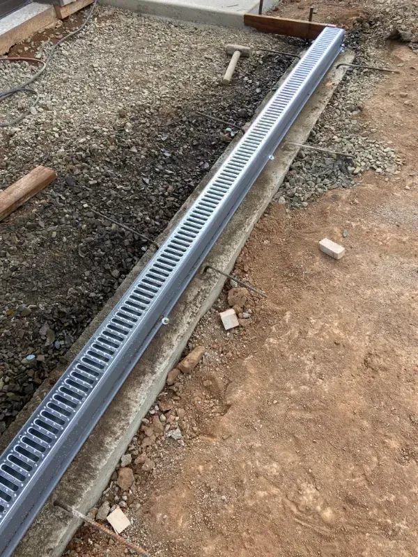 Long metal trench drain installed in a gravel and dirt construction area