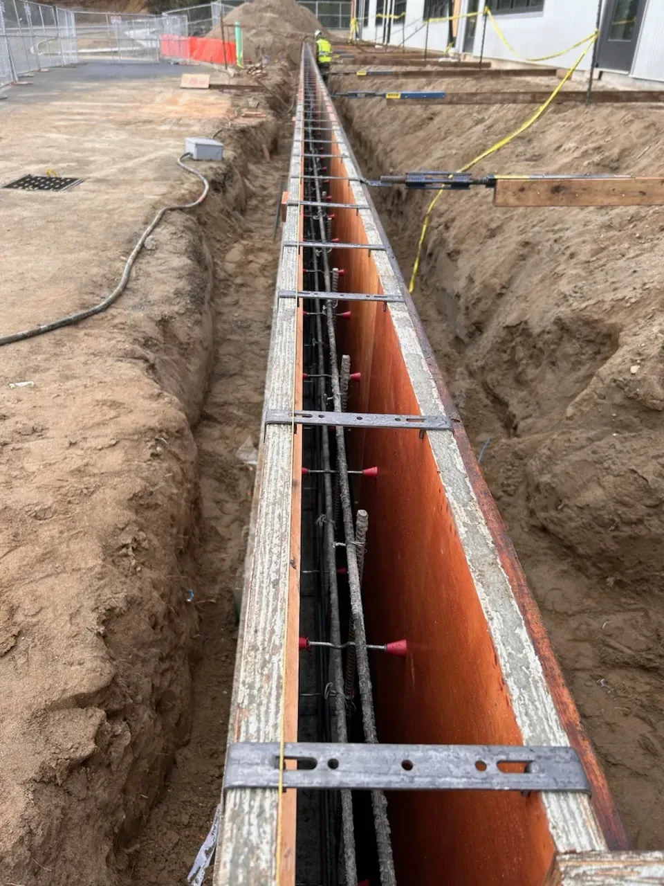 Trench with steel rebar and orange conduit laid for underground utility installation at a construction site