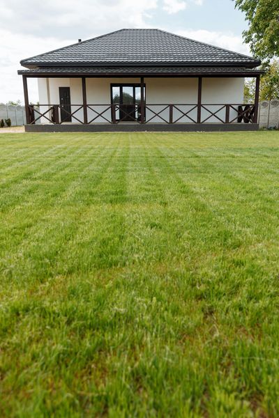 Single-story house with a dark roof and porch, viewed across a large green lawn