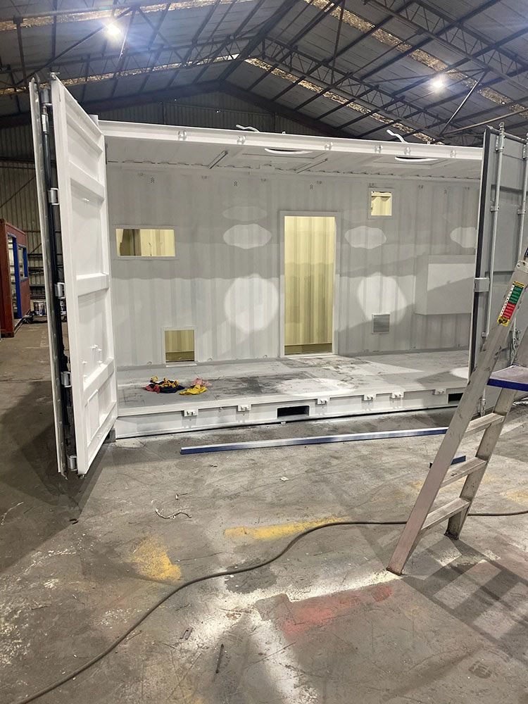 A Shipping Container Is Being Painted In A Warehouse With A Ladder — Oz Shipping Containers in Teralba, NSW