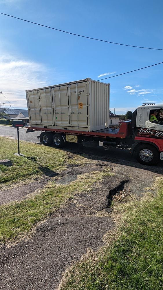A Tow Truck Is Carrying A Shipping Container Down A Road — Oz Shipping Containers in Teralba, NSW