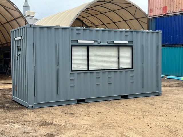 A Gray Shipping Container With A Window Is Sitting In A Dirt Field — Oz Shipping Containers in Melbourne, VIC