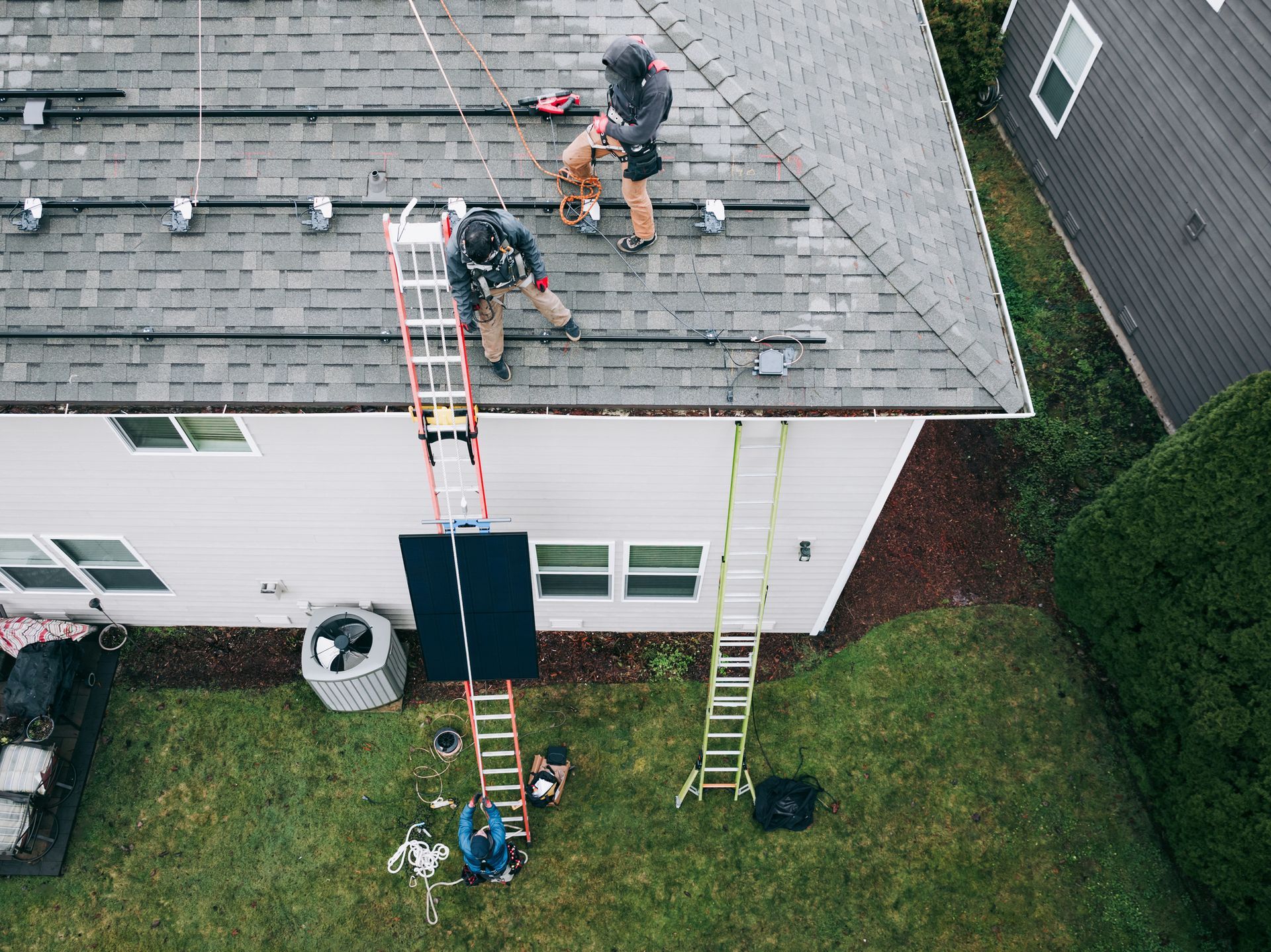 An aerial view of two men installing solar panels on the roof of a house.