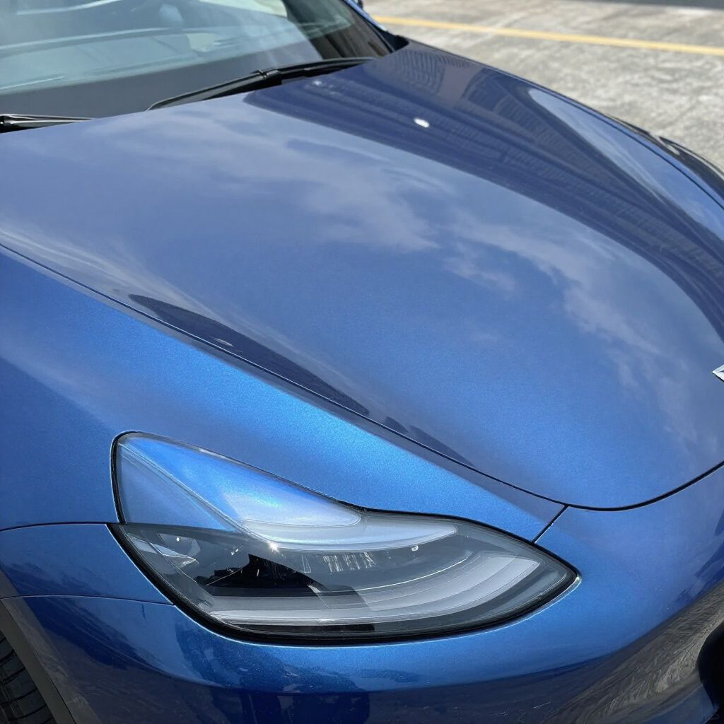 Close-up of a blue car hood and headlight reflecting the sky