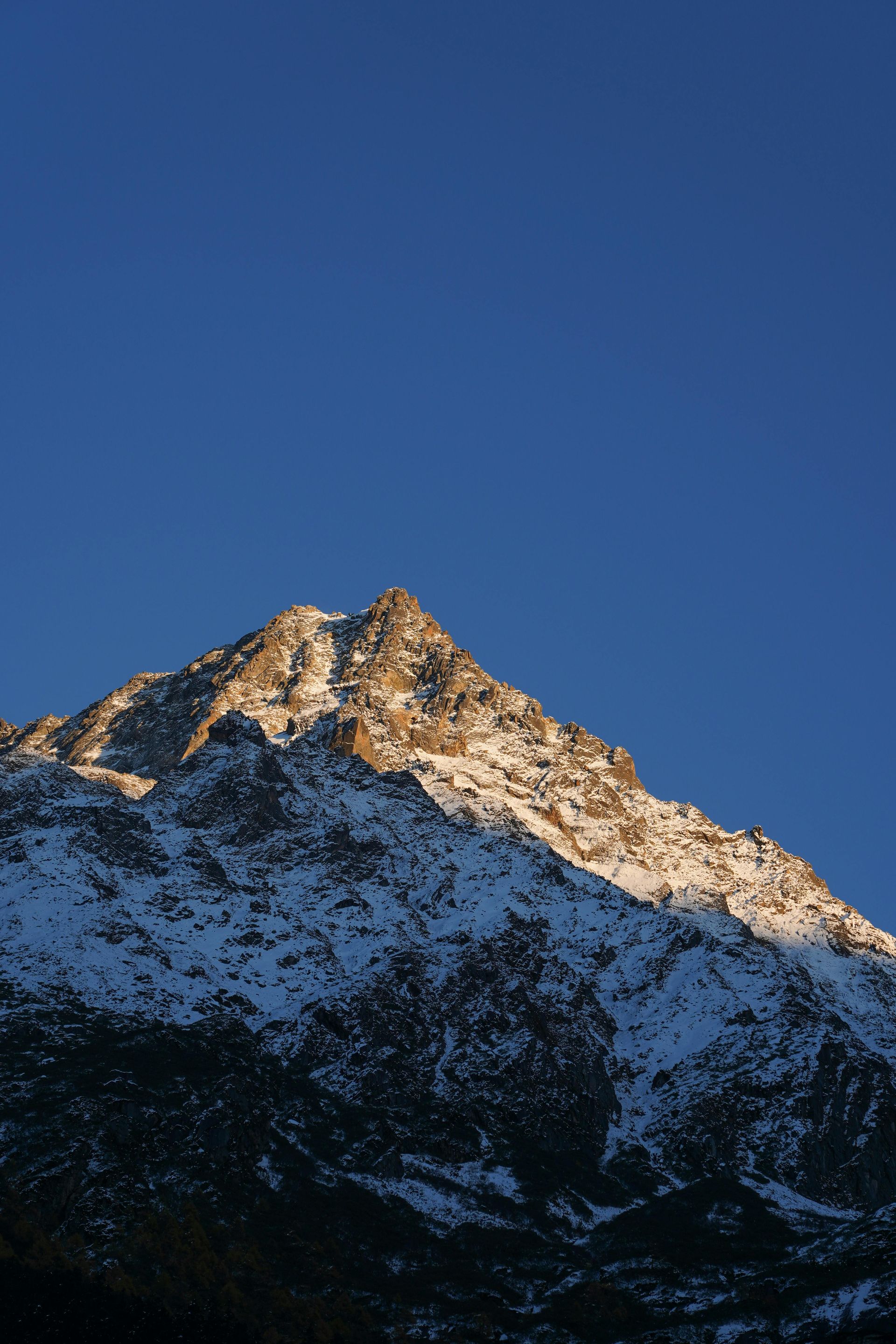 Snowy mountain peak lit by warm sunlight against a clear blue sky