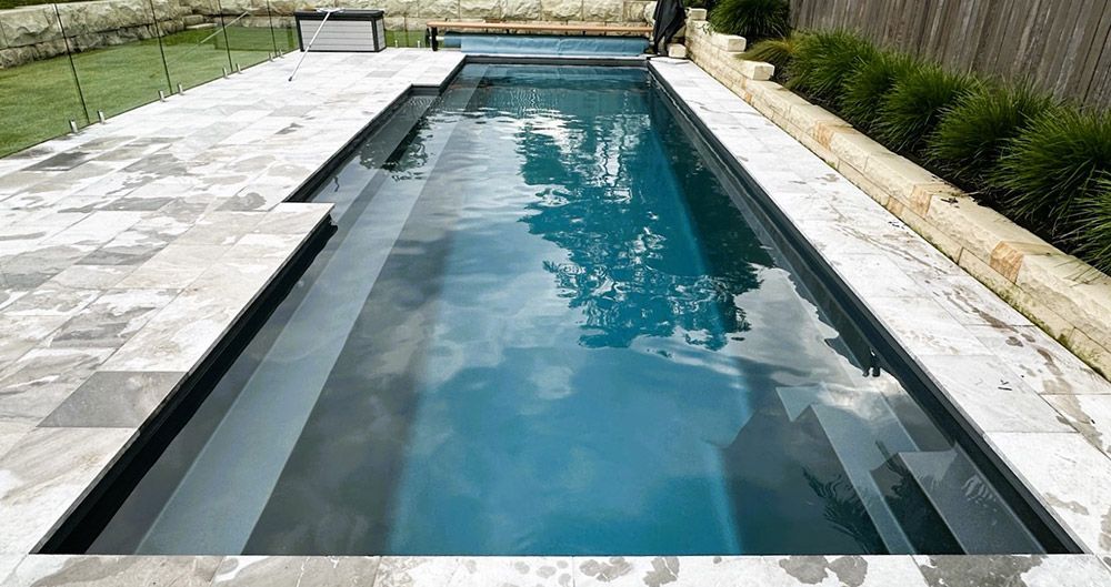 A Large Swimming Pool is Surrounded by a Patio and a Fence — Taree Pool Supplies in Taree, NSW
