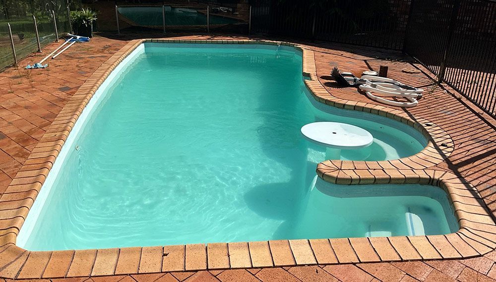 A Large Swimming Pool is Surrounded by Bricks and a Fence — Taree Pool Supplies in Forster, NSW