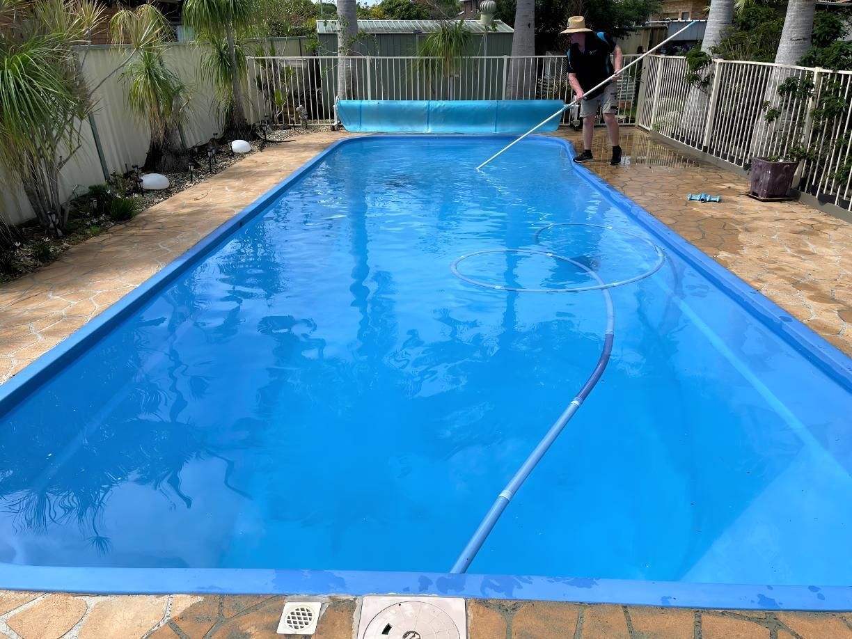 A Man is Cleaning a Large Swimming Pool With a Broom — Taree Pool Supplies in Taree, NSW