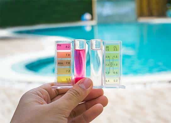 A Person is Holding a Test Tube in Front of a Swimming Pool — Taree Pool Supplies in Taree, NSW
