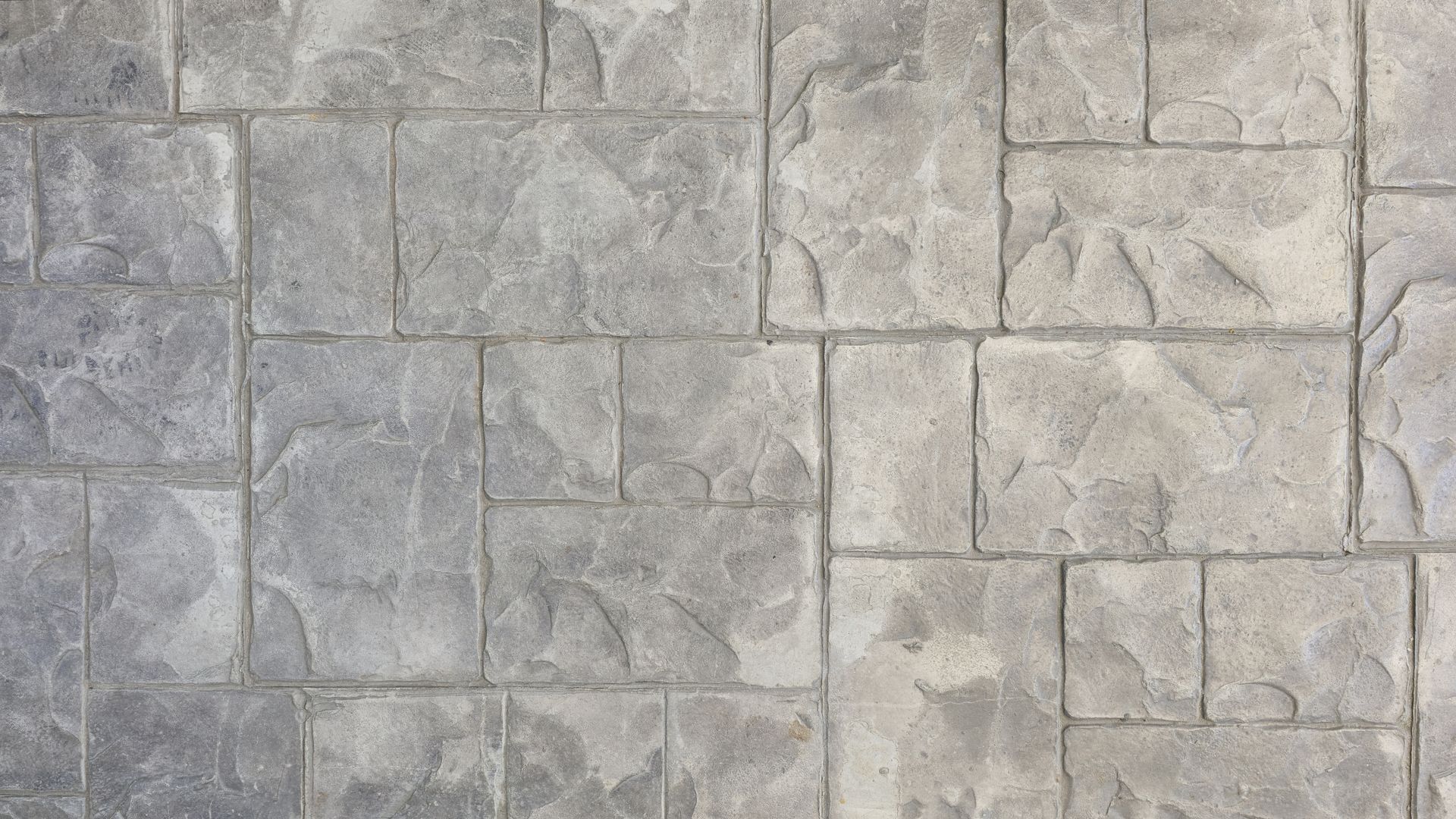 A close-up view of gray, textured concrete paving stones with a grid pattern of rectangular and square tiles. A close-up view of gray, textured concrete paving stones with a grid pattern of rectangular and square tiles.