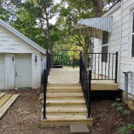 Newly constructed wooden deck and stairs with black metal railings situated between a white garage and a house.