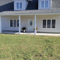 A single-story house with cream siding, gray roof, white porch columns, a central front door, and a green lawn.