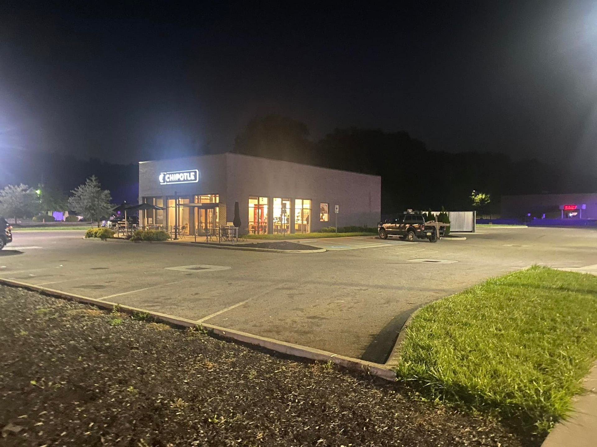 A building with a lot of windows is lit up at night in a parking lot.