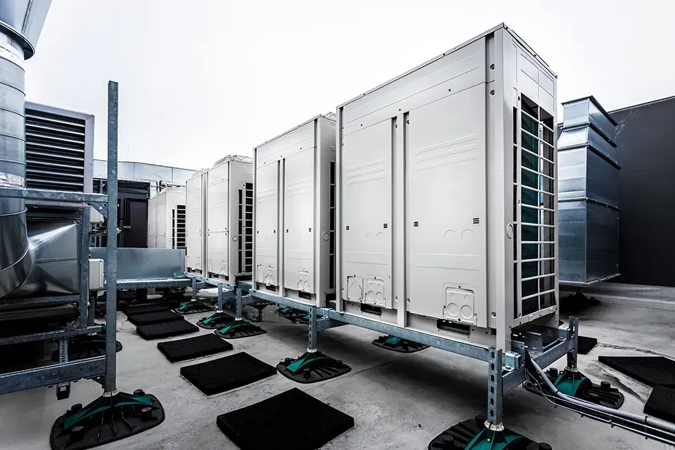 Rooftop HVAC units on platforms with ductwork and metal framing against a cloudy sky.