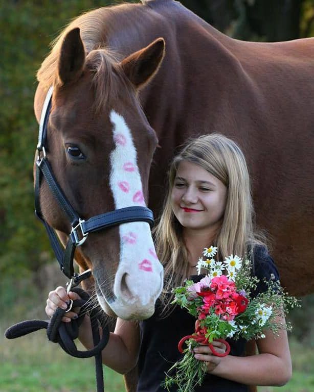 A girl holding a bouquet of flowers next to a horse