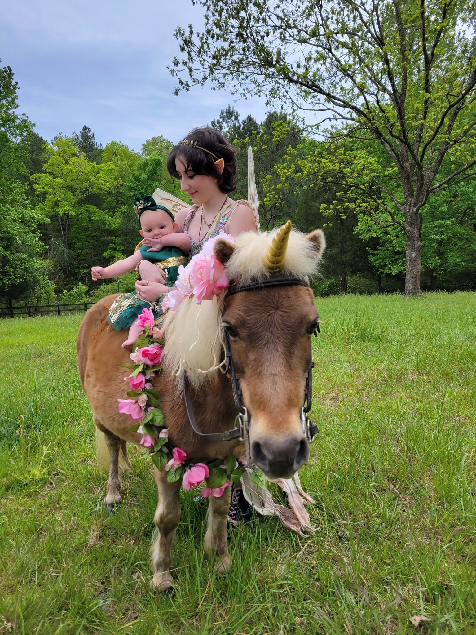 A woman is holding a baby while riding on the back of a pony.