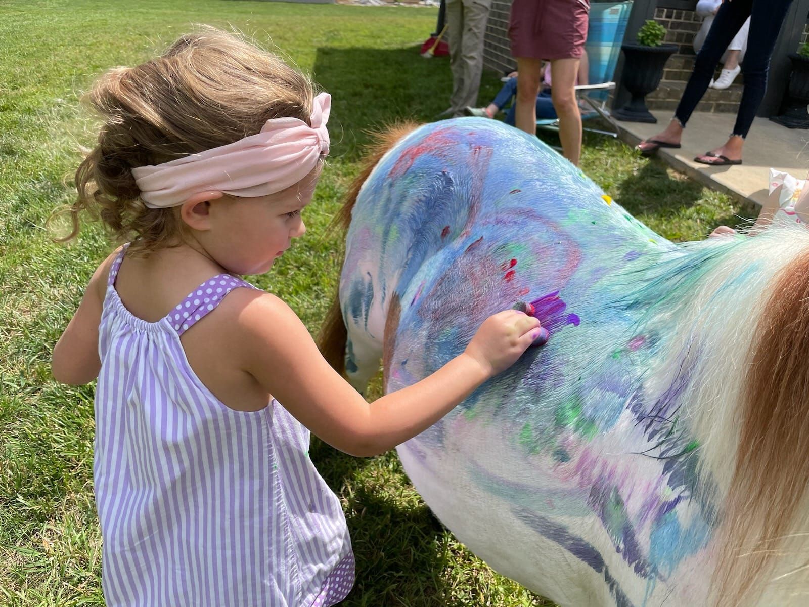A little girl is painting a horse with purple paint.