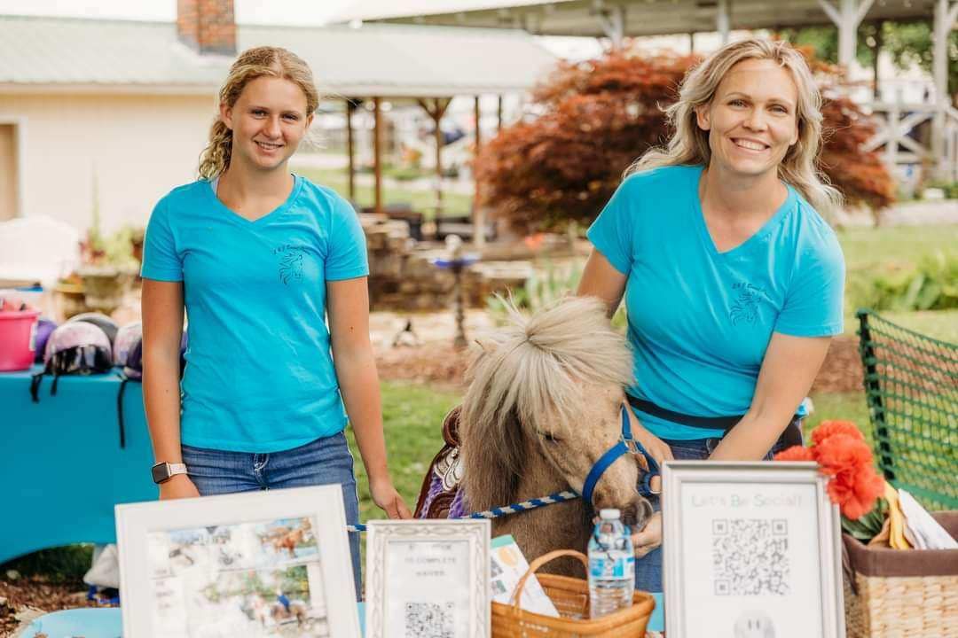 Two women are standing next to a pony at a table.
