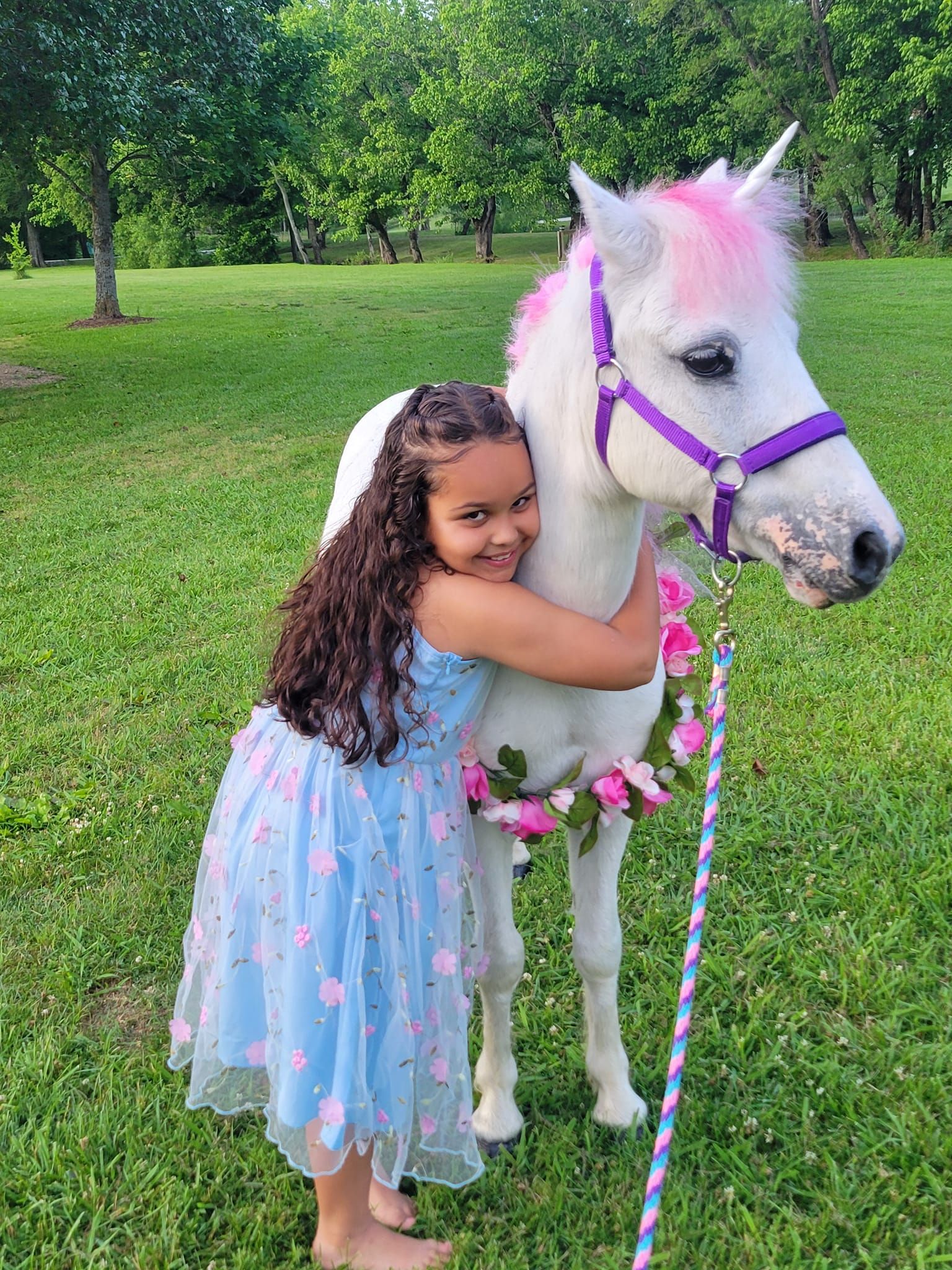 A little girl in a blue dress is hugging a white unicorn.