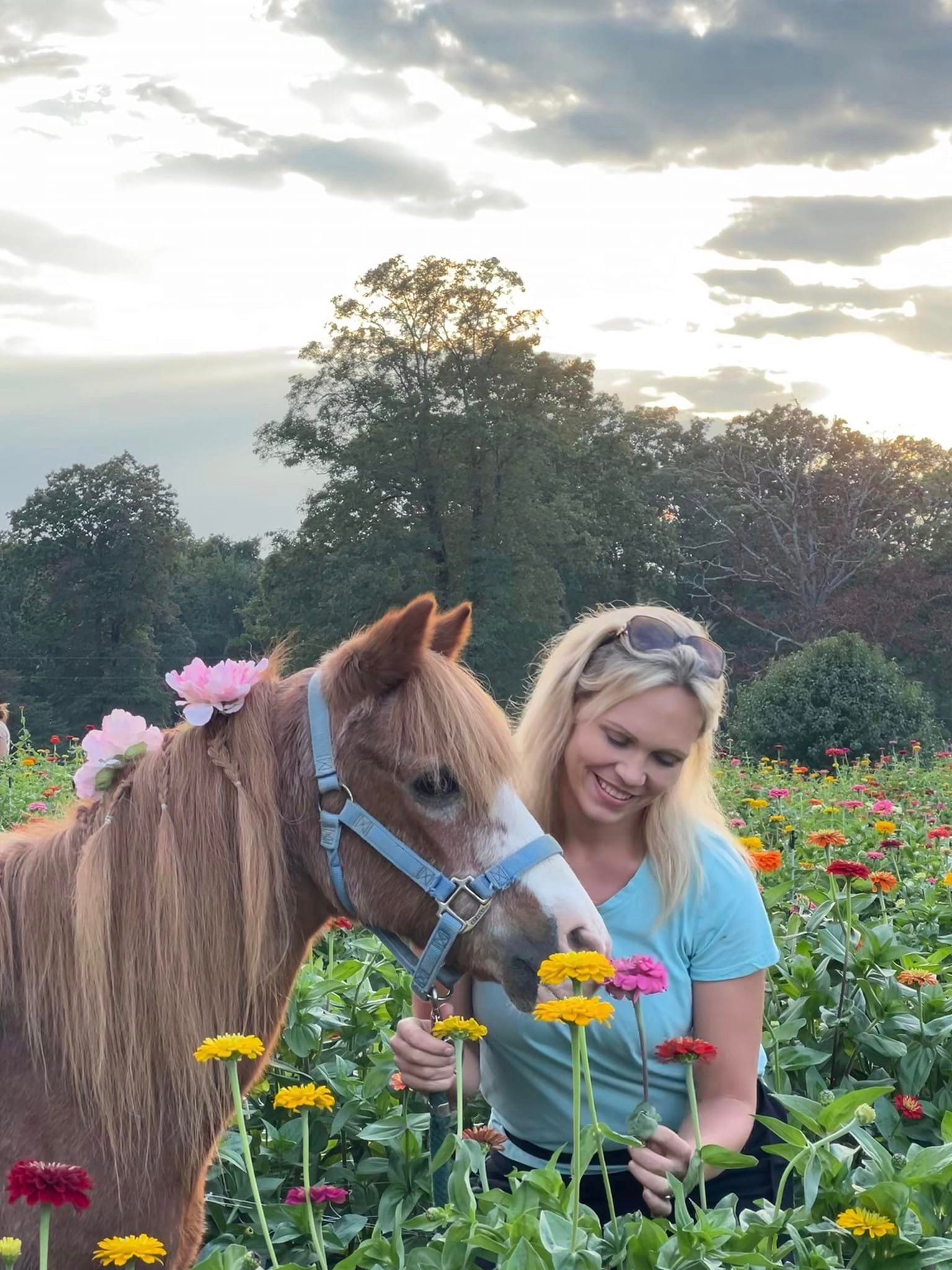 A woman is standing next to a horse in a field of flowers.