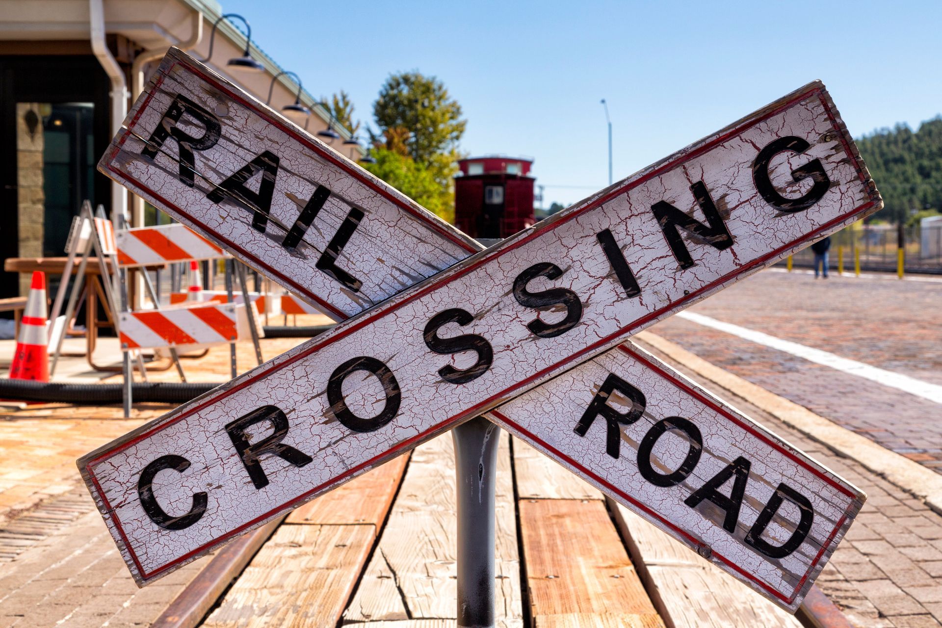 Railroad crossing sign, weathered, white text on brown boards, outdoors.